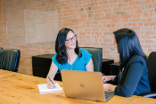 2 women talking with a laptop sitting with a conference table